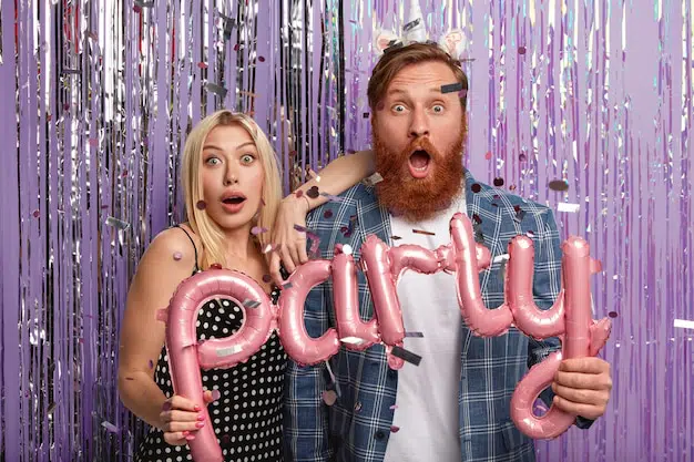 A smiling couple posing in a photo booth, holding "PARTY" letter balloons.